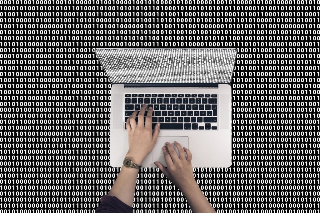 Hands typing on laptop with binary code background